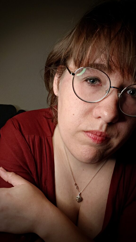 up-close face of a young woman wearing big round glasses and a red dress and a visible gold necklace